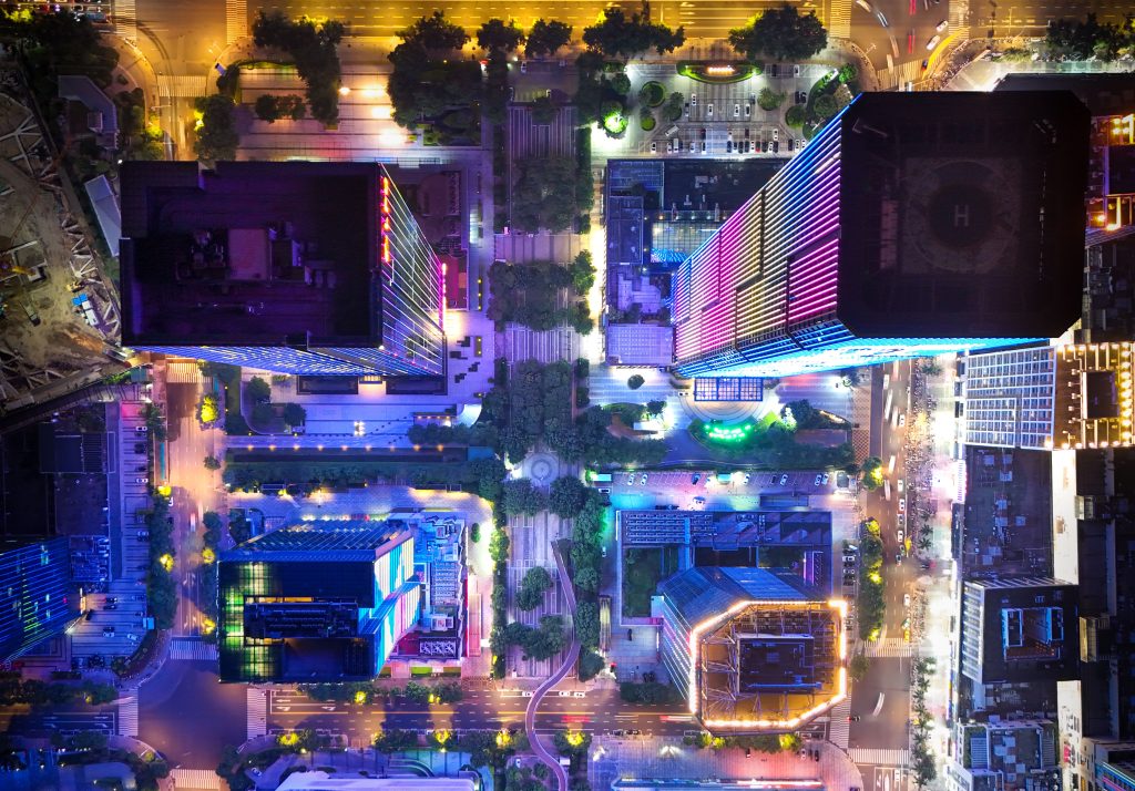 Stunning aerial view of illuminated city buildings at night with colorful lights.
